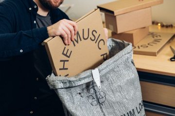 Ein Mann verpackt ein schmales Paket mit der Aufschrift THE MUSIC in eine Versandtasche.