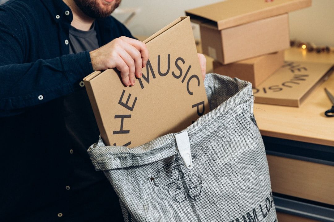 Ein Mann verpackt ein schmales Paket mit der Aufschrift THE MUSIC in eine Versandtasche.